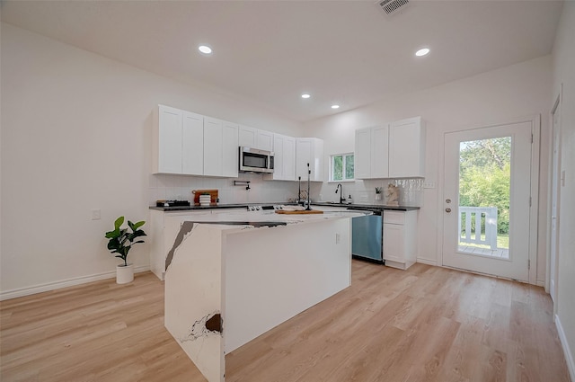 kitchen featuring a kitchen island, tasteful backsplash, white cabinetry, stainless steel appliances, and light hardwood / wood-style flooring