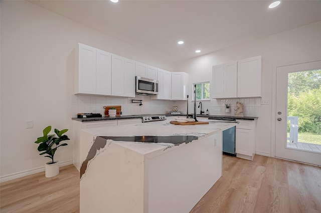 kitchen featuring a kitchen island with sink, white cabinetry, light hardwood / wood-style floors, and decorative backsplash