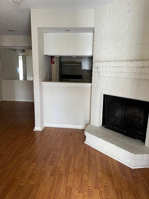 unfurnished living room featuring a brick fireplace, wood-type flooring, and a textured ceiling