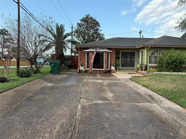 view of front of house featuring brick siding, a front yard, fence, and a shingled roof