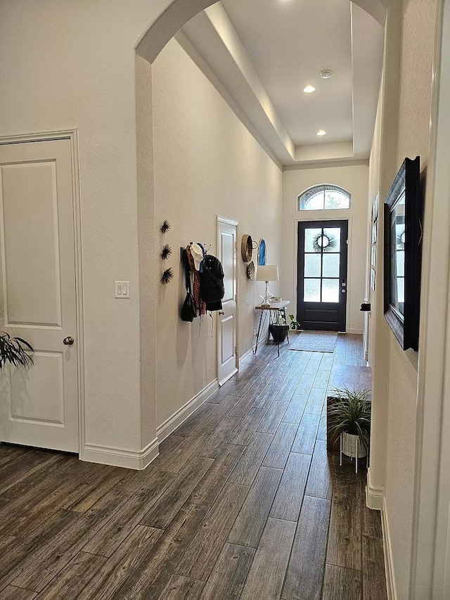 entryway with arched walkways, dark wood finished floors, and baseboards