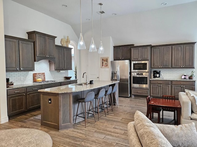 kitchen with decorative light fixtures, appliances with stainless steel finishes, open floor plan, a sink, and an island with sink