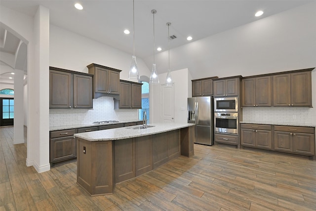 16715 Ramsay Cascades Dr, Humble, TX 77346 - kitchen featuring stainless steel appliances, a sink, arched walkways, high vaulted ceiling, and dark wood-style floors
