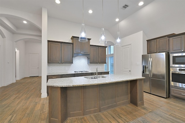 16715 Ramsay Cascades Dr, Humble, TX 77346 - kitchen featuring stainless steel appliances, a sink, arched walkways, backsplash, and dark brown cabinets