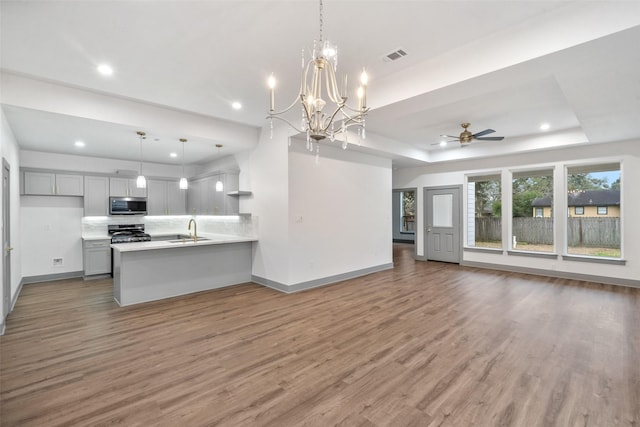 kitchen featuring appliances with stainless steel finishes, sink, gray cabinetry, hanging light fixtures, and a raised ceiling