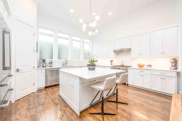 kitchen featuring appliances with stainless steel finishes, light hardwood / wood-style flooring, hanging light fixtures, a breakfast bar area, and white cabinetry