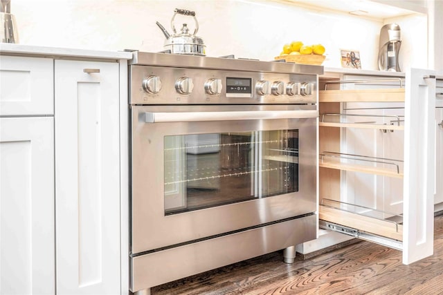 details with stainless steel stove, white cabinetry, and hardwood / wood-style floors