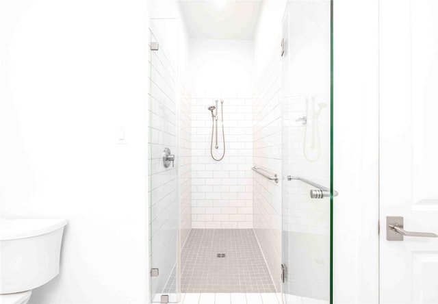 bathroom featuring a shower with door and toilet