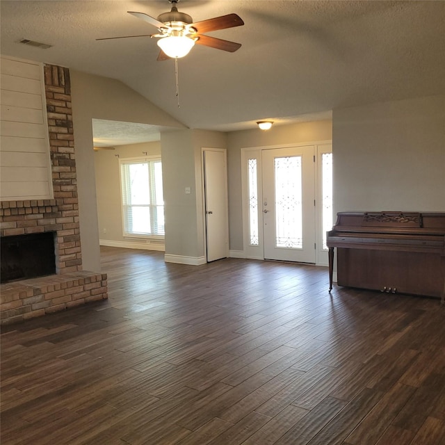 living room with ceiling fan, a textured ceiling, dark hardwood / wood-style flooring, a brick fireplace, and vaulted ceiling