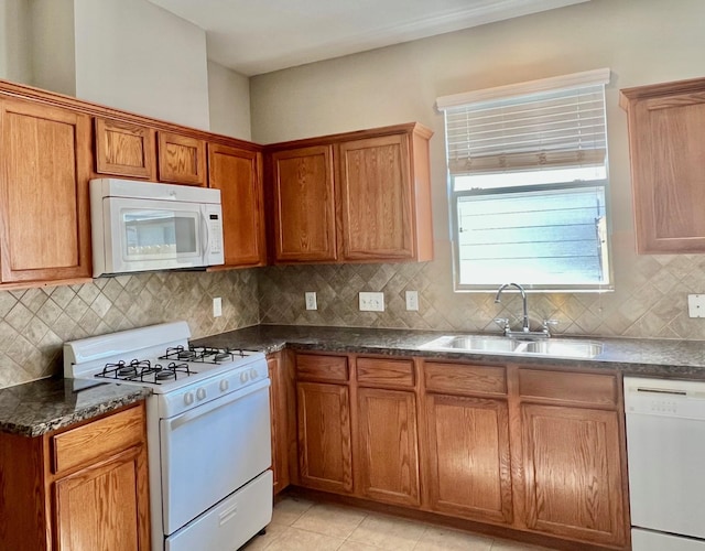 kitchen featuring sink, white appliances, tasteful backsplash, light tile patterned flooring, and dark stone counters