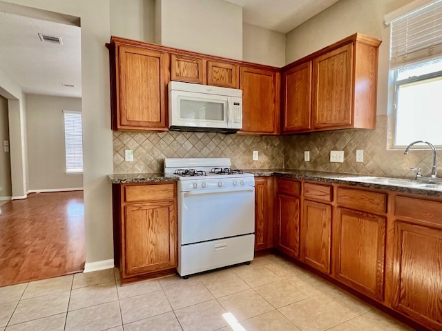 kitchen featuring sink, dark stone countertops, backsplash, light tile patterned floors, and white appliances