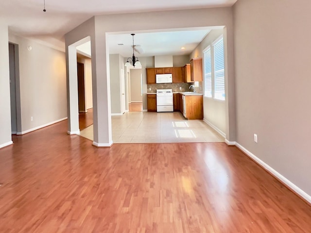 kitchen featuring decorative light fixtures, sink, backsplash, stove, and light hardwood / wood-style floors