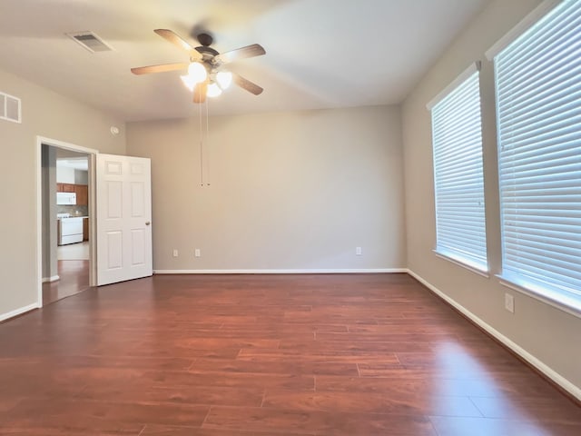 empty room with a wealth of natural light, dark hardwood / wood-style floors, and ceiling fan