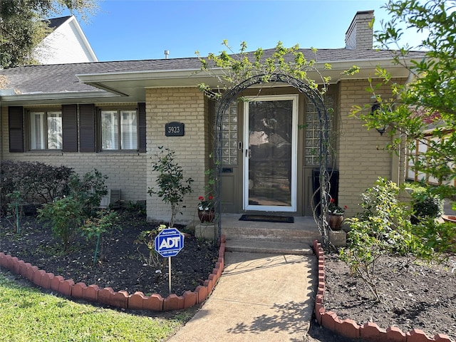 doorway to property with roof with shingles and brick siding