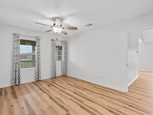 spare room with a textured ceiling, light wood-style flooring, visible vents, baseboards, and a ceiling fan