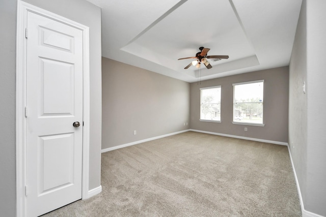 carpeted spare room with a tray ceiling and ceiling fan