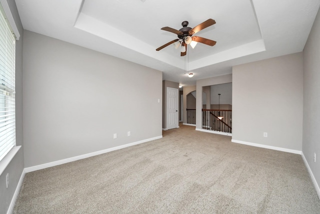 carpeted empty room with a raised ceiling and ceiling fan