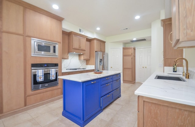 kitchen with sink, appliances with stainless steel finishes, a center island, light stone countertops, and decorative backsplash