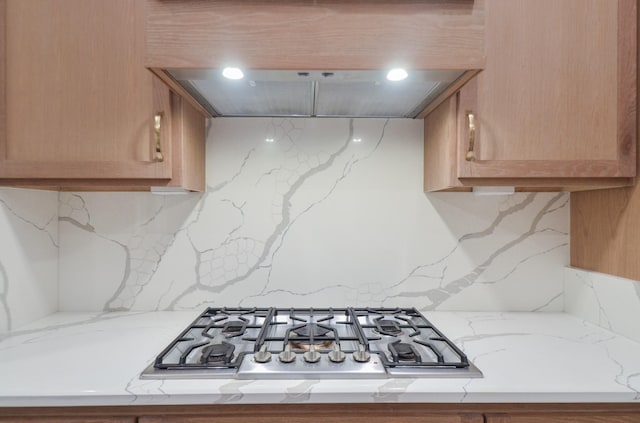 kitchen with light stone counters, tasteful backsplash, exhaust hood, and stainless steel gas cooktop