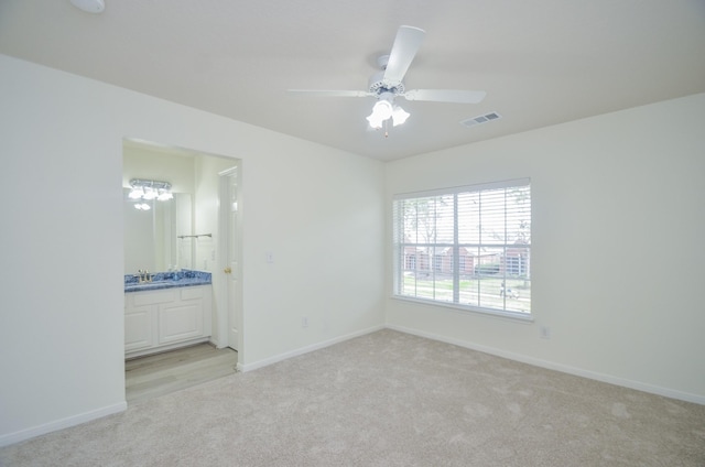 unfurnished bedroom with ensuite bathroom, sink, light colored carpet, and ceiling fan