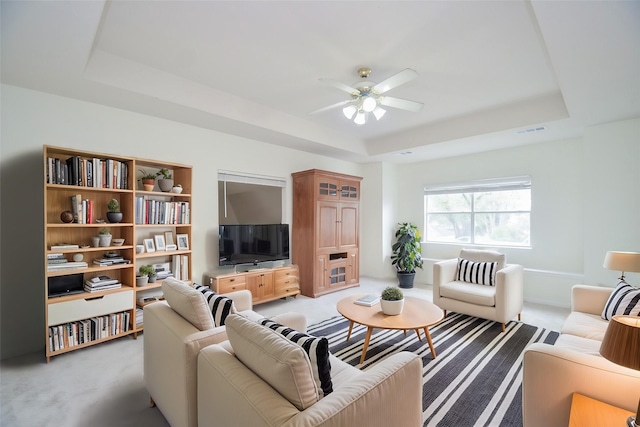 living room featuring ceiling fan, light colored carpet, and a tray ceiling