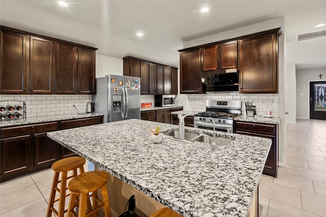 kitchen featuring sink, a breakfast bar area, stainless steel appliances, light stone countertops, and an island with sink