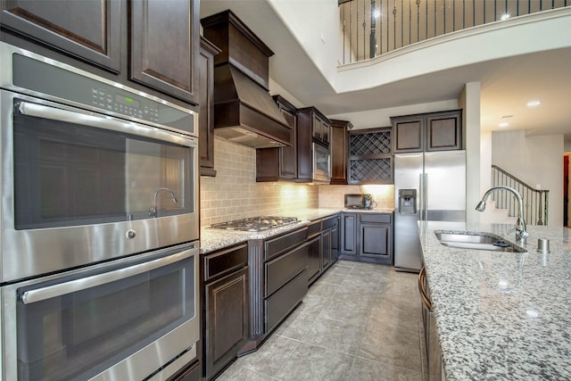 kitchen with dark brown cabinetry, sink, light stone counters, appliances with stainless steel finishes, and decorative backsplash