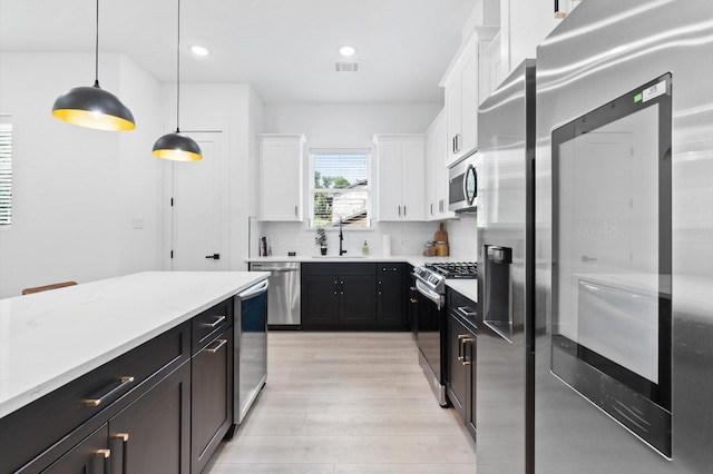 501 E 39th St, Houston, TX 77022 - kitchen featuring appliances with stainless steel finishes, dark cabinets, white cabinetry, light wood-type flooring, and decorative backsplash