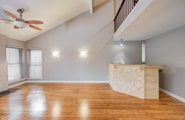 unfurnished living room with high vaulted ceiling, baseboards, a ceiling fan, and wood finished floors