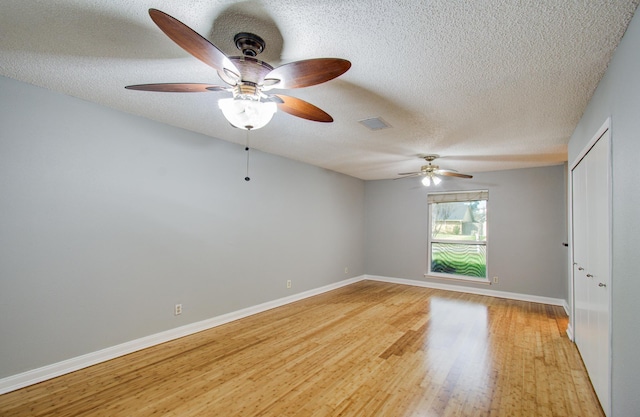spare room with a textured ceiling, light wood-type flooring, visible vents, and ceiling fan