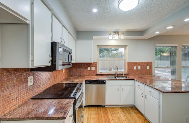 kitchen featuring a peninsula, appliances with stainless steel finishes, a sink, and a textured ceiling