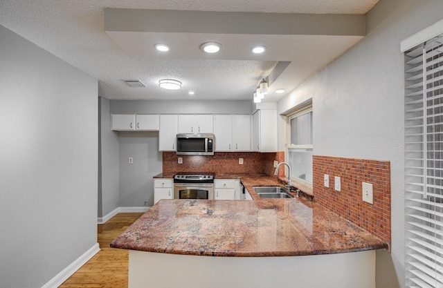 kitchen featuring dark stone counters, a sink, stainless steel appliances, backsplash, and white cabinetry