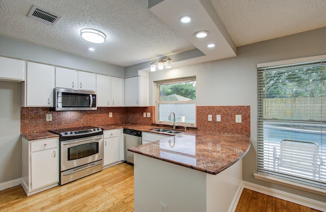 kitchen with light wood finished floors, a peninsula, a textured ceiling, visible vents, and appliances with stainless steel finishes