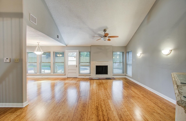 unfurnished living room with a ceiling fan, a fireplace with raised hearth, baseboards, lofted ceiling, and visible vents