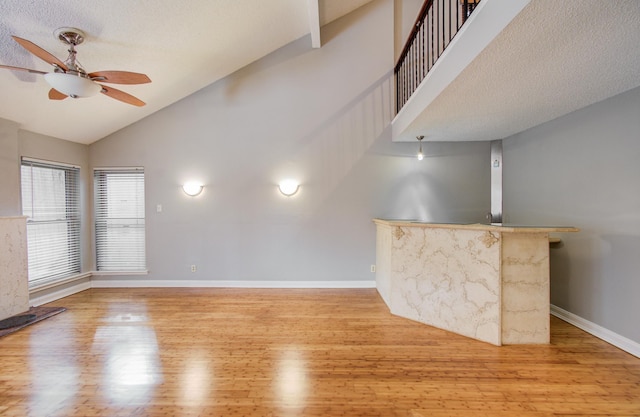 unfurnished living room with high vaulted ceiling, baseboards, a ceiling fan, and wood finished floors