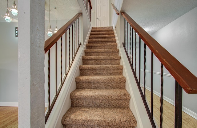 stairs with baseboards, wood finished floors, and a textured ceiling