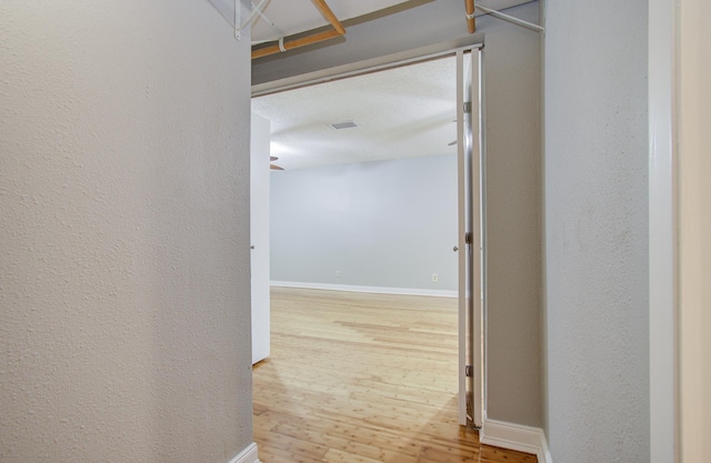 corridor with baseboards, wood finished floors, and visible vents