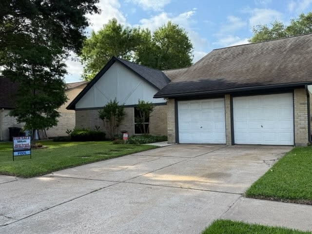 view of front of property with brick siding, an attached garage, a front lawn, and driveway
