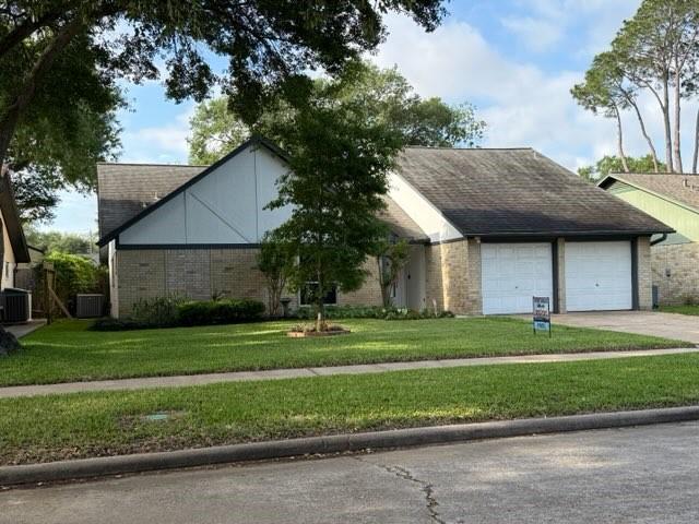 view of front of home with cooling unit, concrete driveway, roof with shingles, a front yard, and a garage