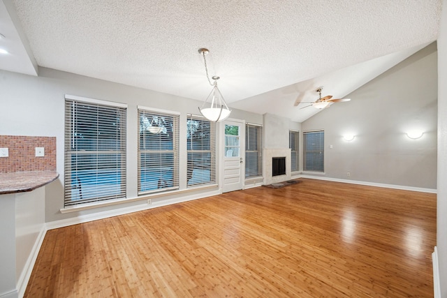 22403 Elsinore Dr, Katy, TX 77450 - unfurnished living room with wood finished floors, a fireplace with raised hearth, a textured ceiling, ceiling fan, and vaulted ceiling
