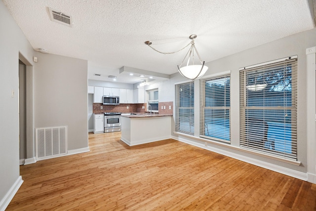 22403 Elsinore Dr, Katy, TX 77450 - kitchen featuring appliances with stainless steel finishes, light wood-style floors, white cabinetry, backsplash, and a textured ceiling