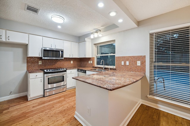 22403 Elsinore Dr, Katy, TX 77450 - kitchen with stainless steel appliances, a peninsula, light wood finished floors, white cabinets, and a textured ceiling
