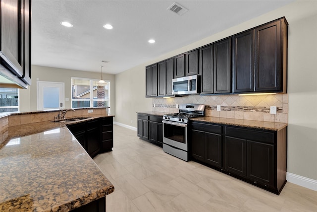 kitchen with dark stone countertops, sink, stainless steel appliances, hanging light fixtures, and tasteful backsplash