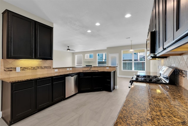 kitchen with sink, pendant lighting, dark stone counters, stainless steel appliances, and kitchen peninsula