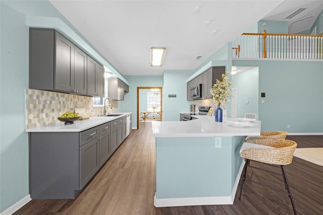 kitchen with a kitchen bar, sink, gray cabinetry, appliances with stainless steel finishes, and kitchen peninsula