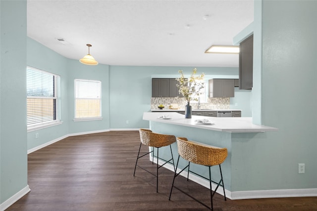 kitchen with gray cabinetry, backsplash, a kitchen bar, kitchen peninsula, and dark wood-type flooring