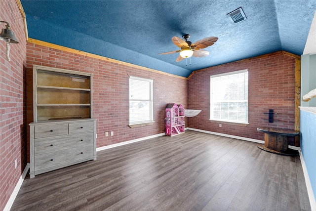 interior space featuring vaulted ceiling, brick wall, dark wood-type flooring, and a textured ceiling