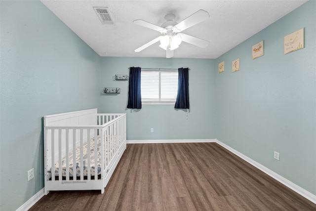 unfurnished bedroom with a textured ceiling, a crib, dark hardwood / wood-style floors, and ceiling fan