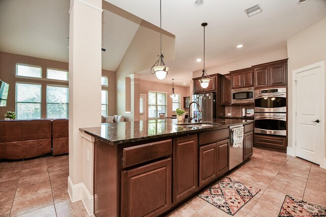 kitchen with visible vents, dark brown cabinets, dark stone countertops, stainless steel appliances, and ornate columns