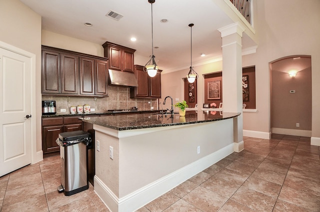 kitchen with visible vents, backsplash, under cabinet range hood, dark stone countertops, and arched walkways